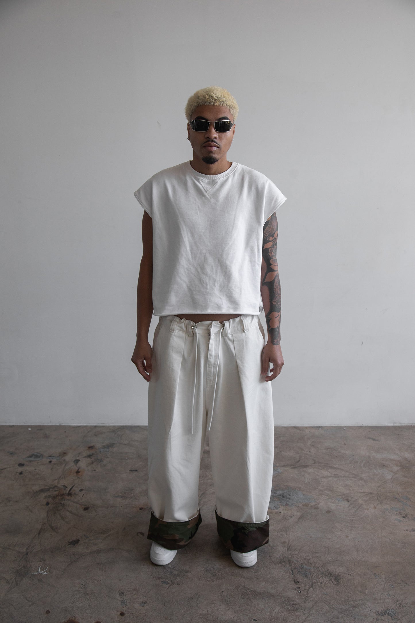 Front view of DACY Studio Uniform Pants in off-white cotton drill with oversized wide-leg fit, adjustable camouflage clip-up hems, elastic drawstring waist and belt loops.