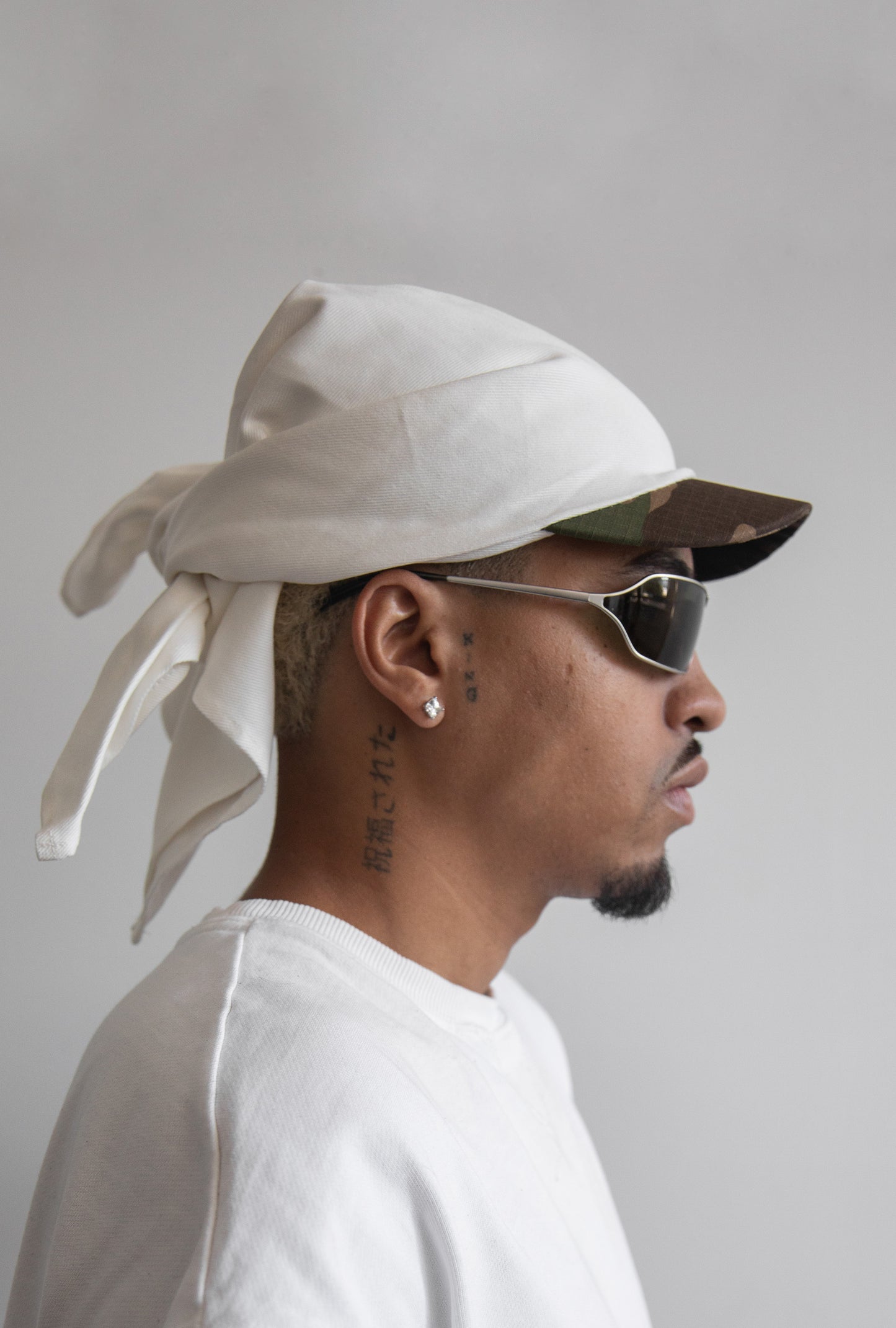 Side view of the DACY Studio Tie Hat in off-white cotton drill with a short camouflage brim, adjustable tie-back design and unisex fit.