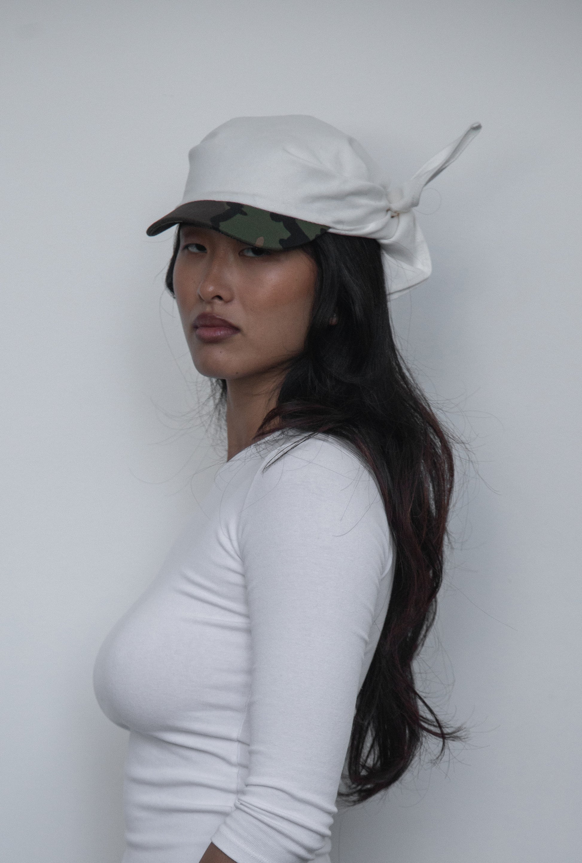 Three-quarter view of the DACY Studio Tie Hat in off-white cotton drill with a short camouflage brim, adjustable tie-back design and unisex fit.