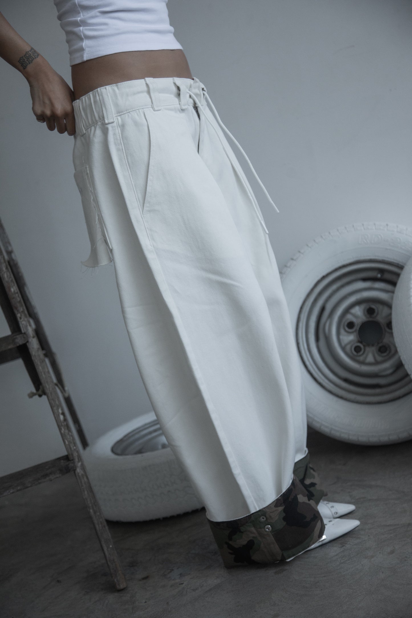 Side view of DACY Studio Uniform Pants in off-white cotton drill with oversized wide-leg fit, adjustable camouflage clip-up hems and elastic drawstring waist.