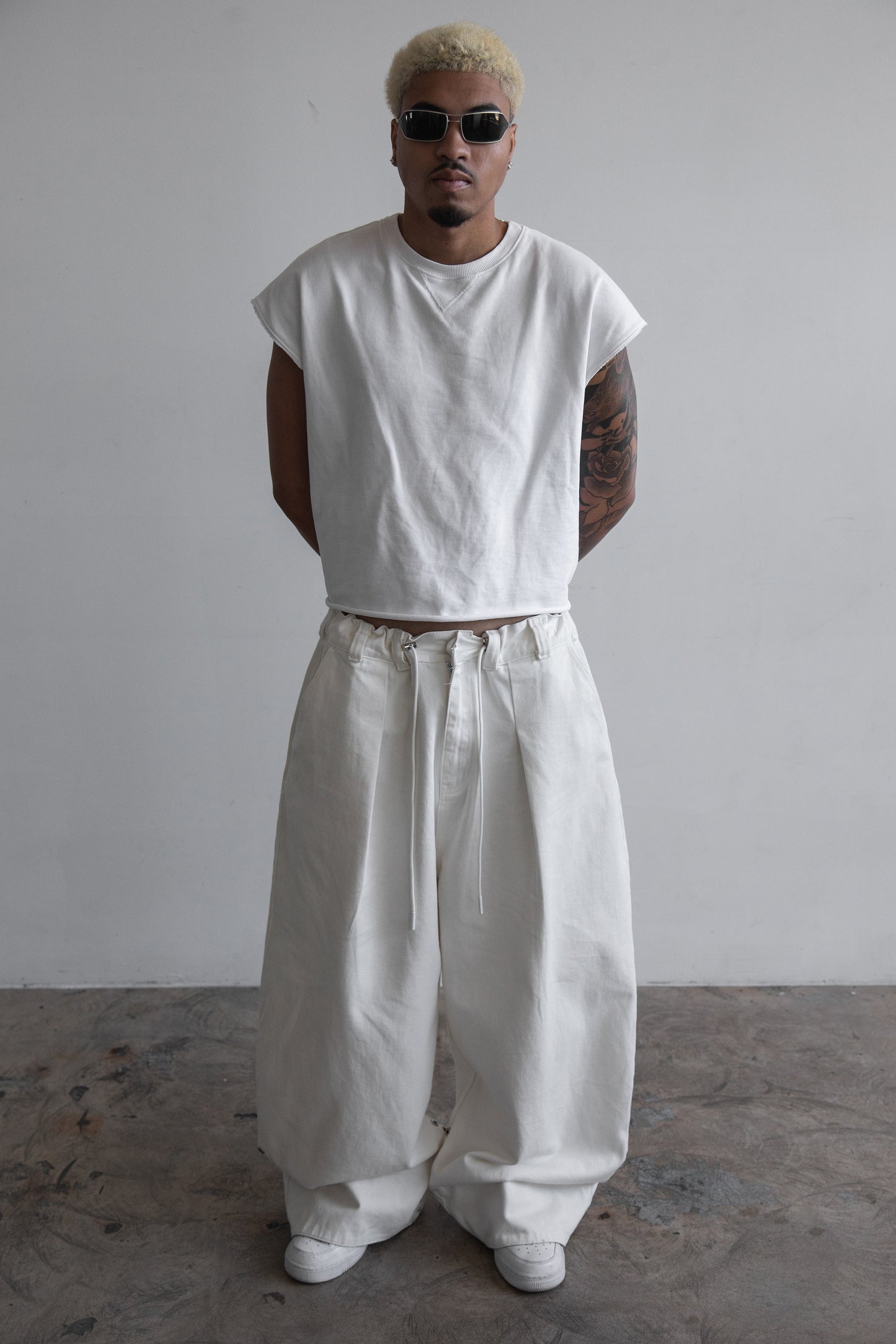 Front view of DACY Studio Uniform Pants in off-white cotton drill with oversized wide-leg fit, adjustable camouflage hems folded down, elastic drawstring waist and belt loops.