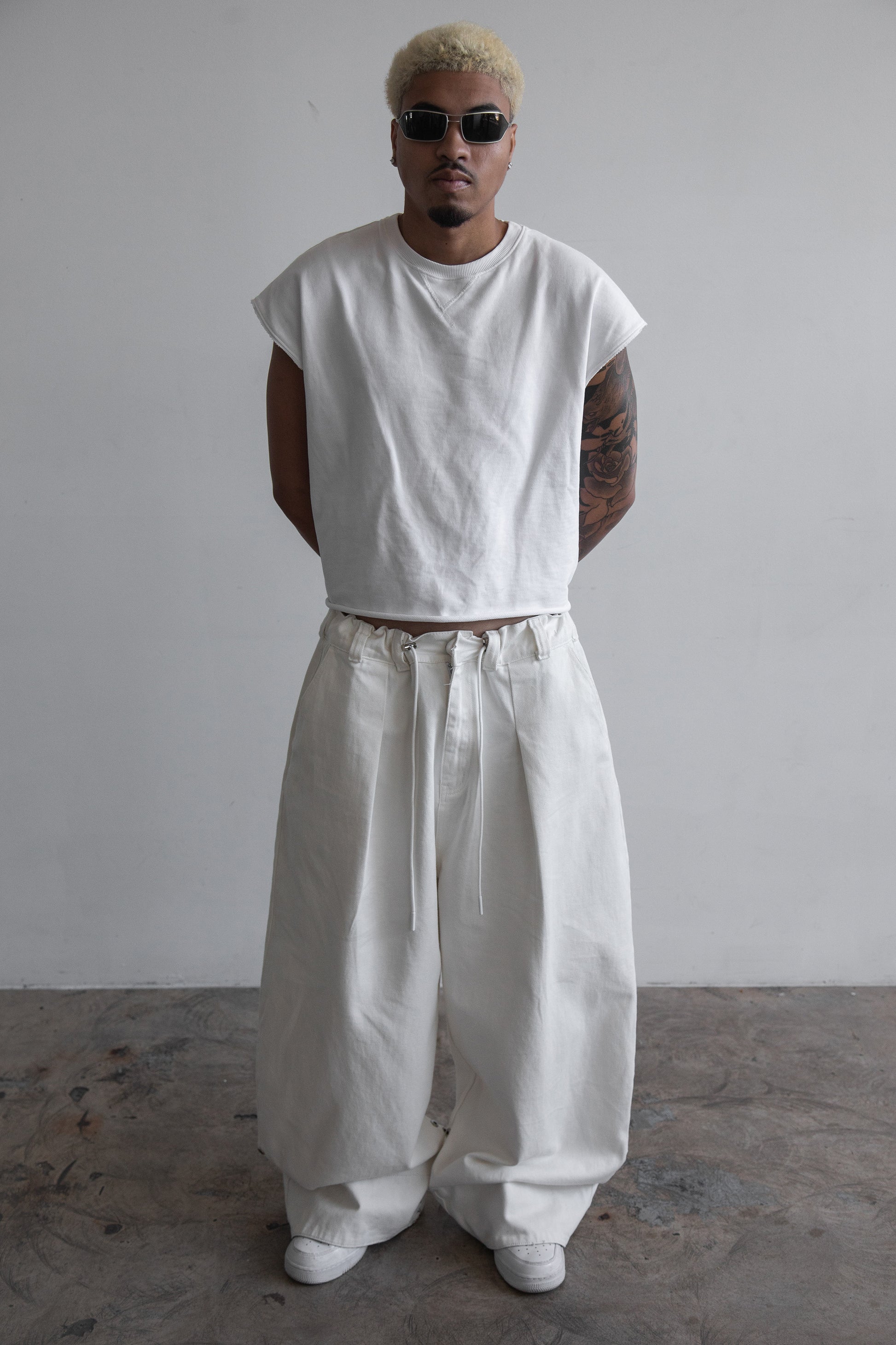 Front view of DACY Studio Uniform Pants in off-white cotton drill with oversized wide-leg fit, adjustable camouflage hems folded down, elastic drawstring waist and belt loops.