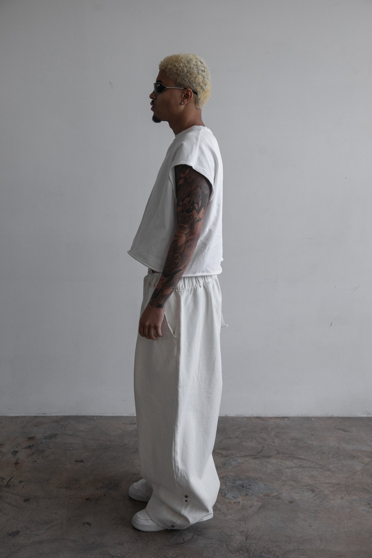 Side view of DACY Studio Uniform Pants in off-white cotton drill with oversized wide-leg fit, adjustable hems in the extended position, elastic drawstring waist and side pockets.