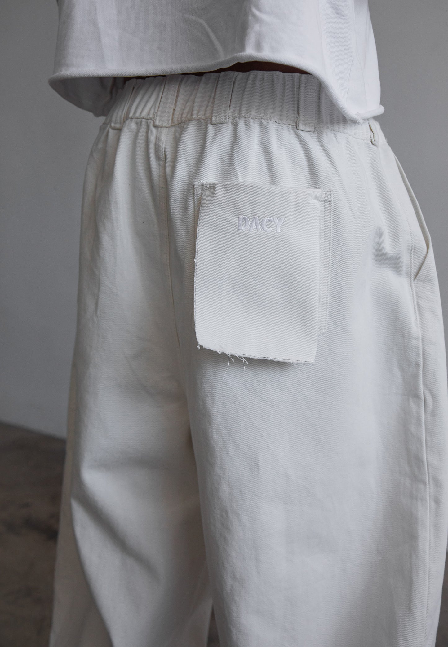 DACY Studio Uniform Pants in off-white with elastic waistband, wide-leg silhouette and embroidery logo patch pocket.