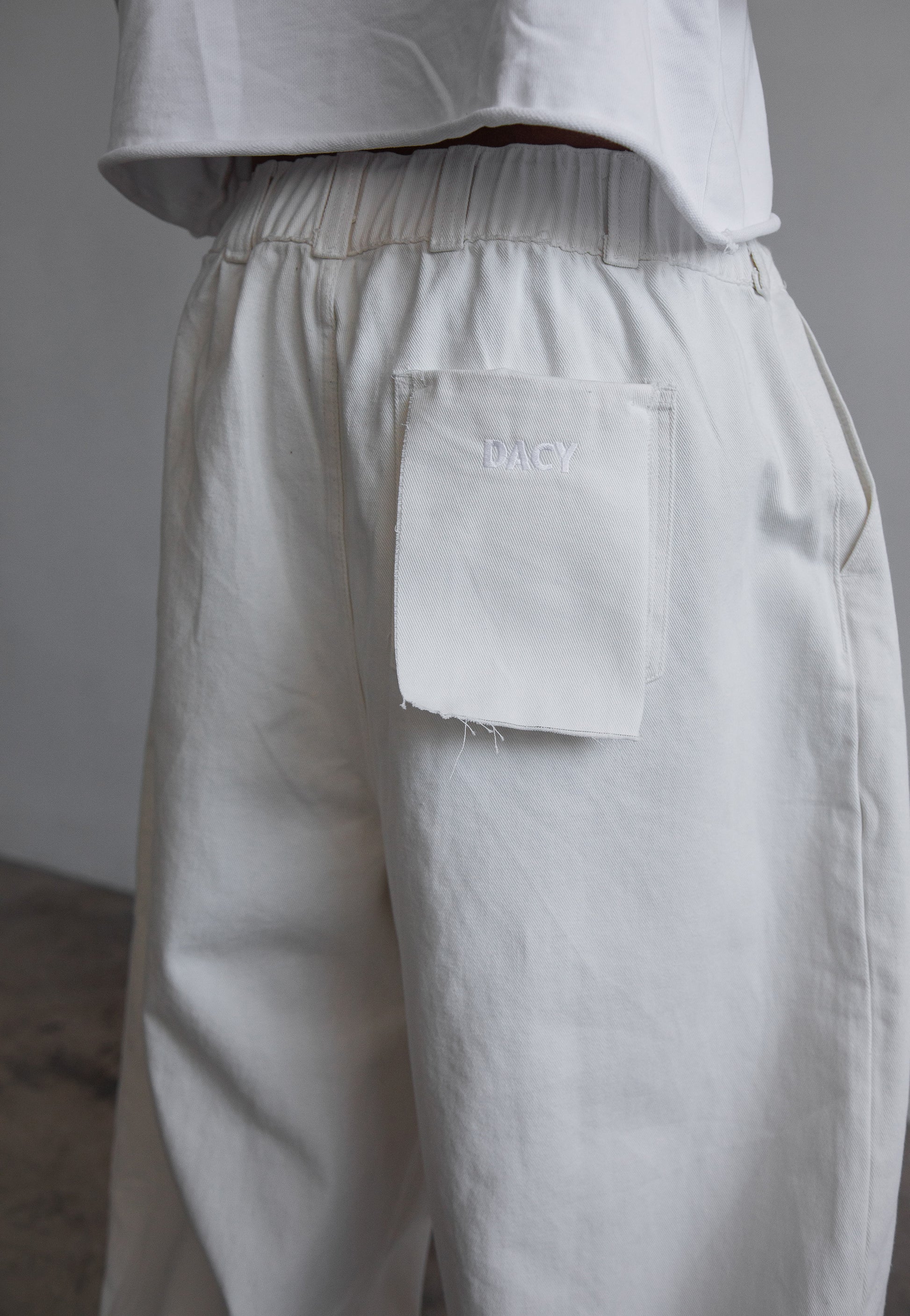 DACY Studio Uniform Pants in off-white with elastic waistband, wide-leg silhouette and embroidery logo patch pocket.